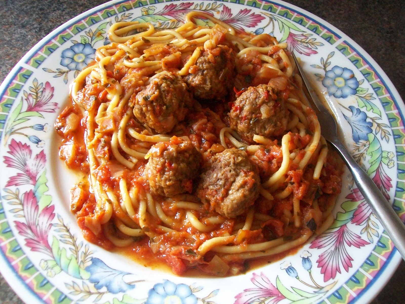 Spaghetti with meatballs in tomato sauce on a colorful floral ceramic plate, close-up view.