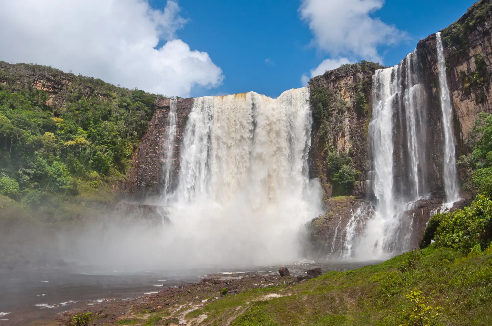 A wide waterfall cascades over a tall cliff surrounded by forest.